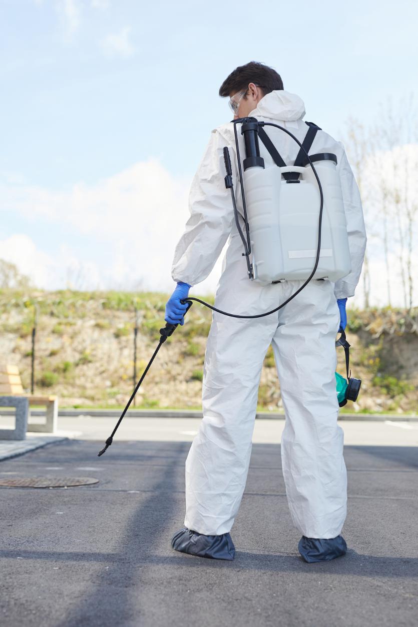 Pest control technician with backpack sprayer treating outdoor area