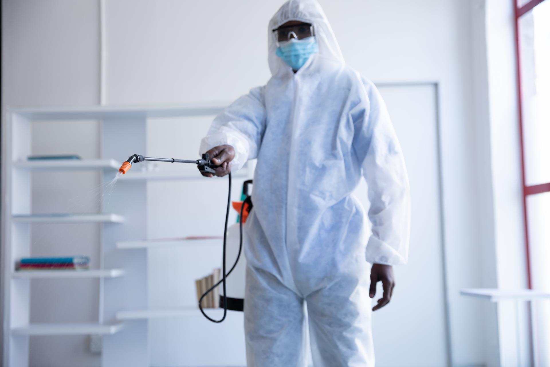 Pest control technician in protective suit spraying treatment in office